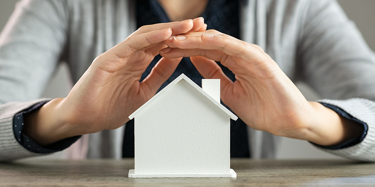 Close up of young woman hands protecting a model of house on tab